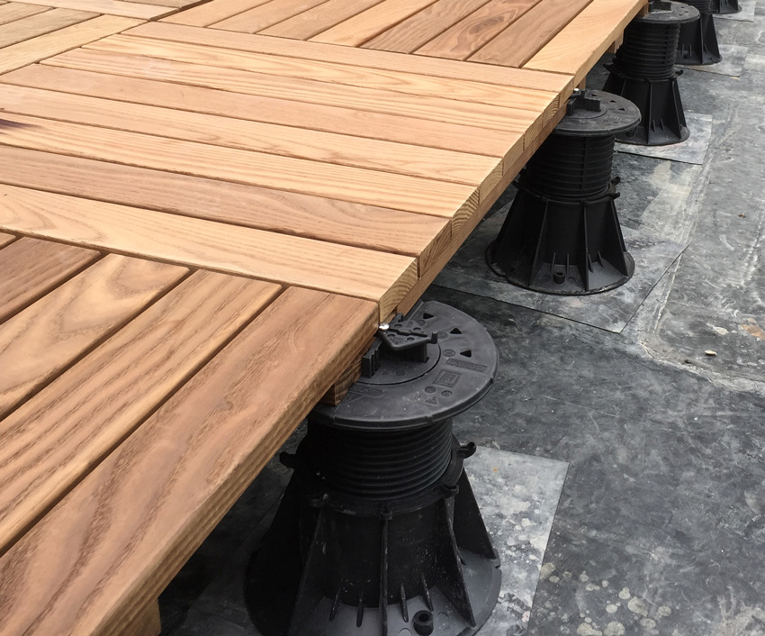 Thermally modified wood tiles are set onto pedestals on a rooftop terrace.