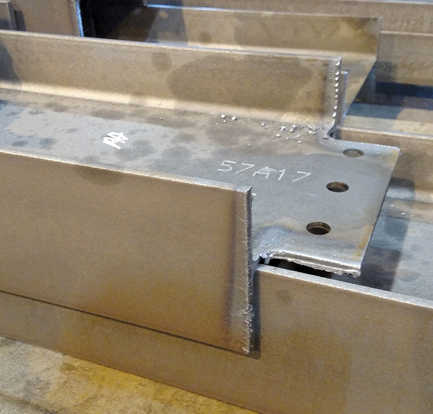 Pictured is a steel beam, recently cut to size and the ends coped per the standard requirements of the AISC Code of Standard Practice for structural steel. The edges have not been ground smooth. Etched numbers and heat marks are visible from the fabrication process. This member is not specified to meet AESS finishes.