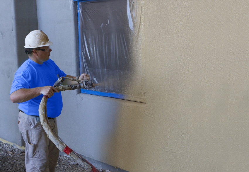 Photo of a man applying stucco with a pump.